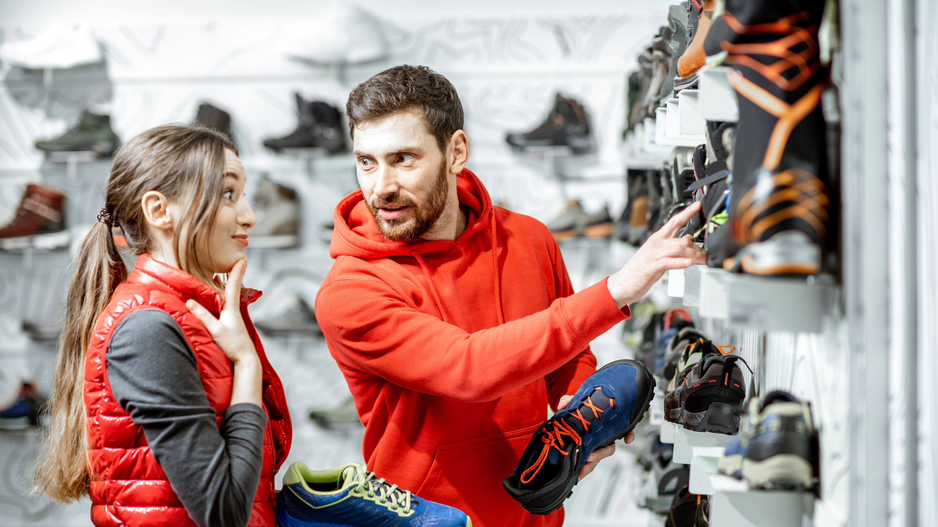 A man and woman selecting shoes from a shop, with numerous shoes neatly arranged on shelves around them.
