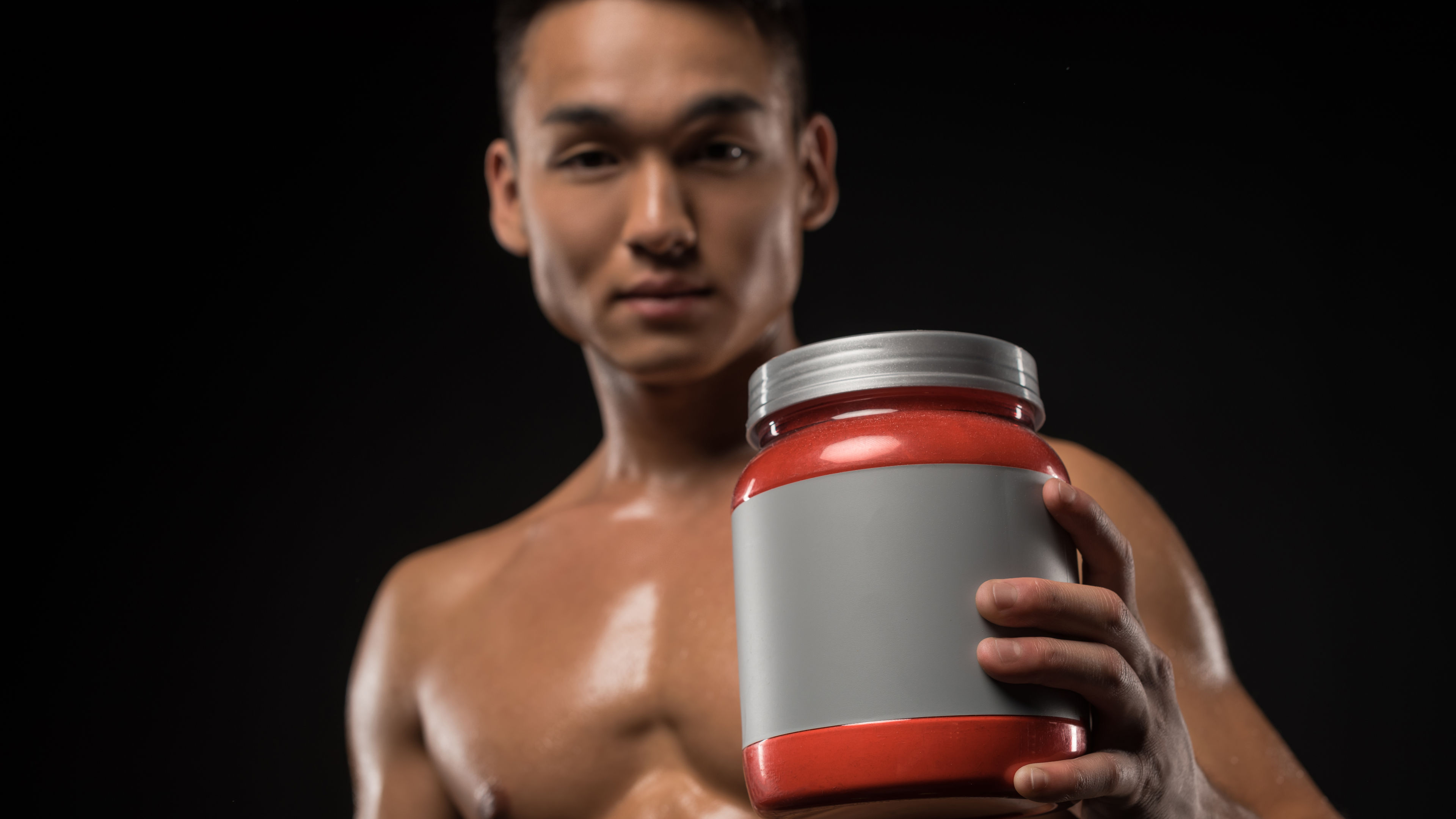 Pandangan dekat seorang atlet Asia memegang balang protein dengan label kosong.