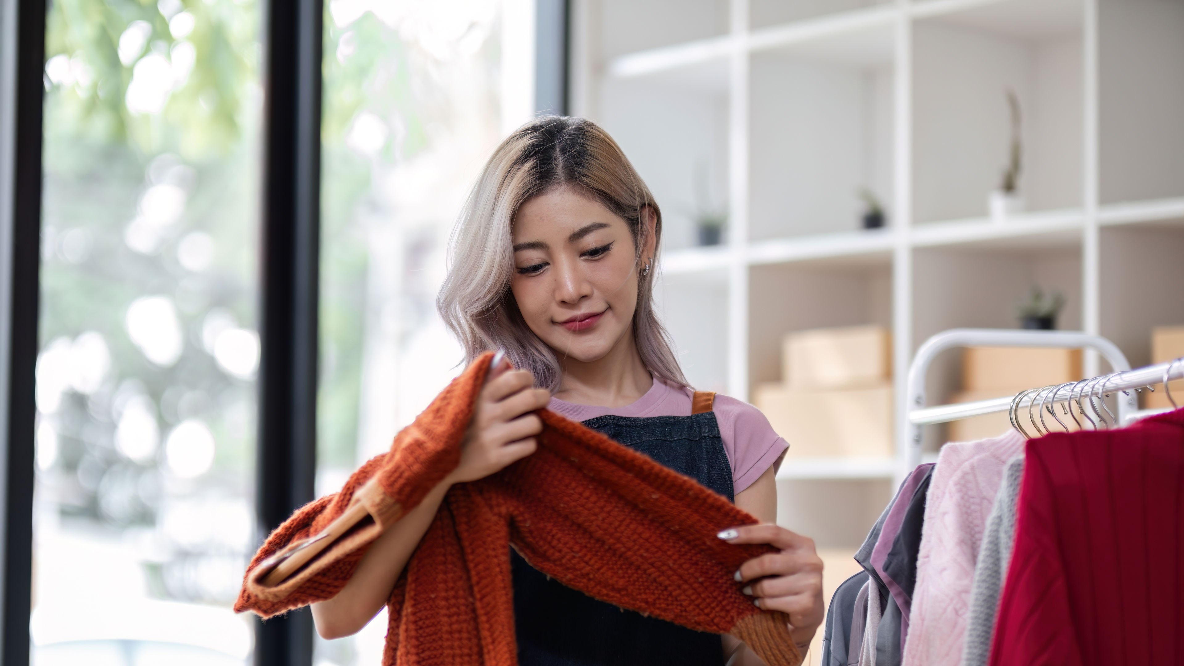 Woman examining an orange knitted sweater in a clothing store.