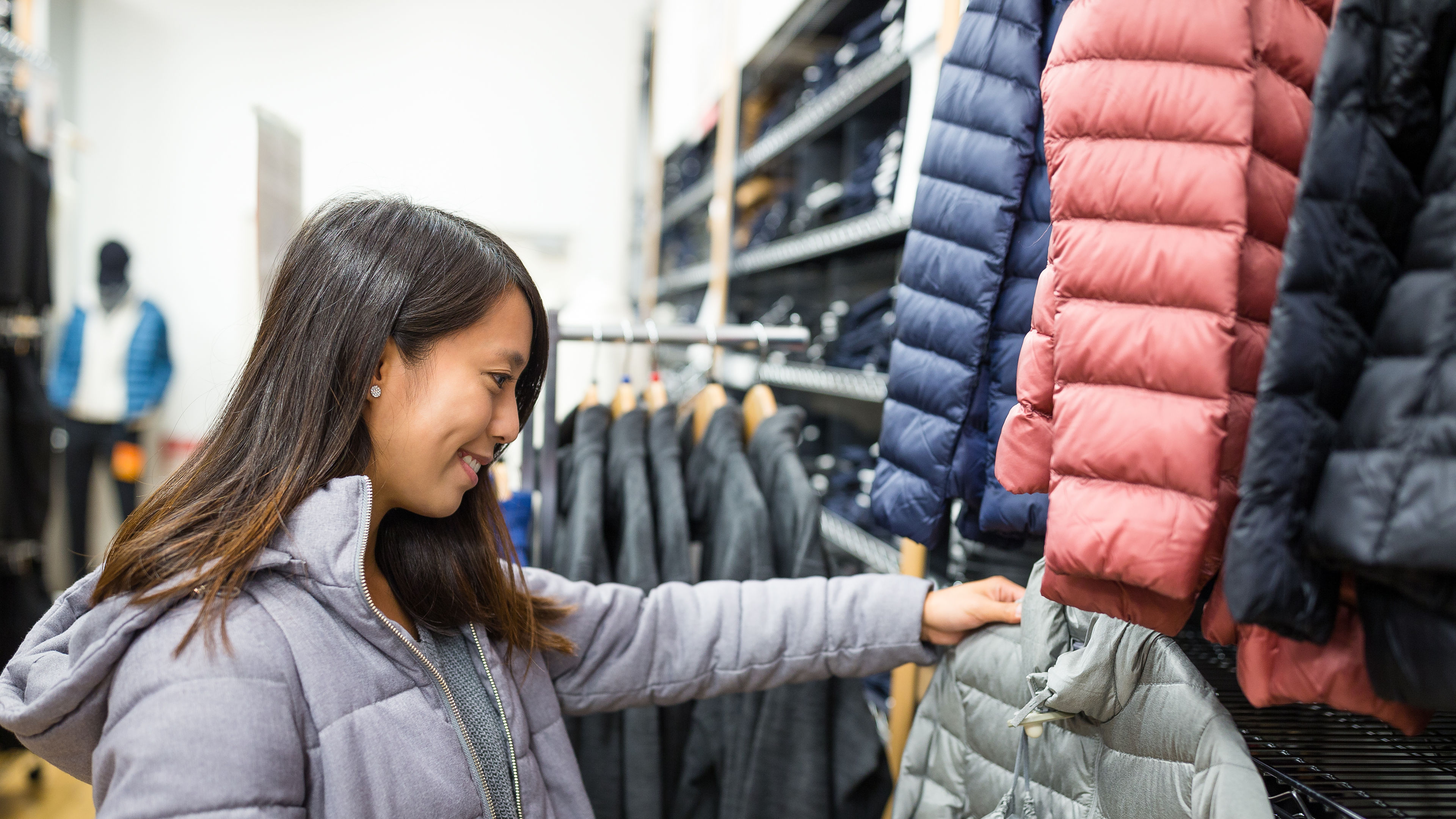 A smiling woman looking at jackets in a clothing store, thoughtfully picking one as she shops.