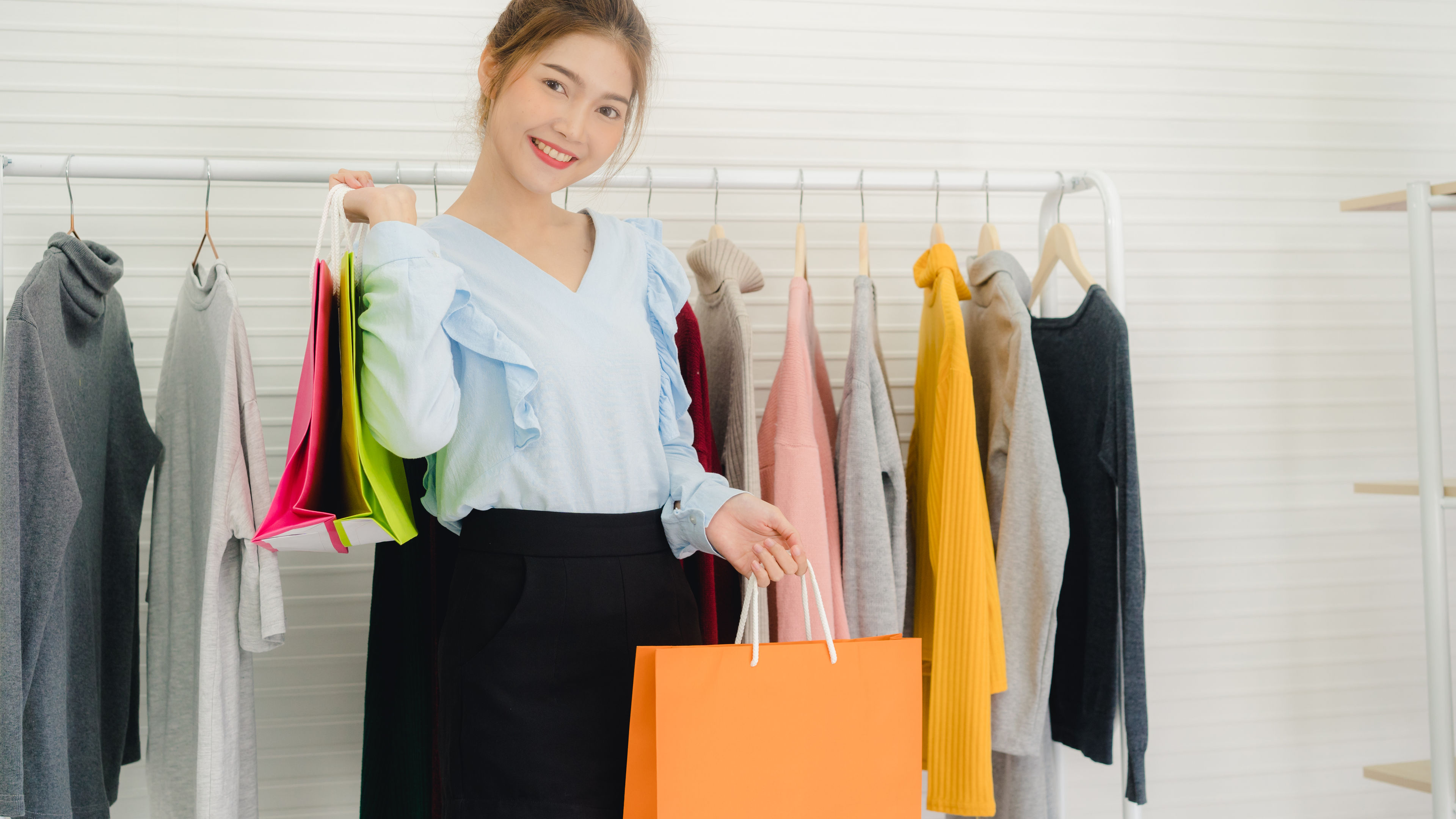 Asian woman with shopping bags Infront of rack of clothes.