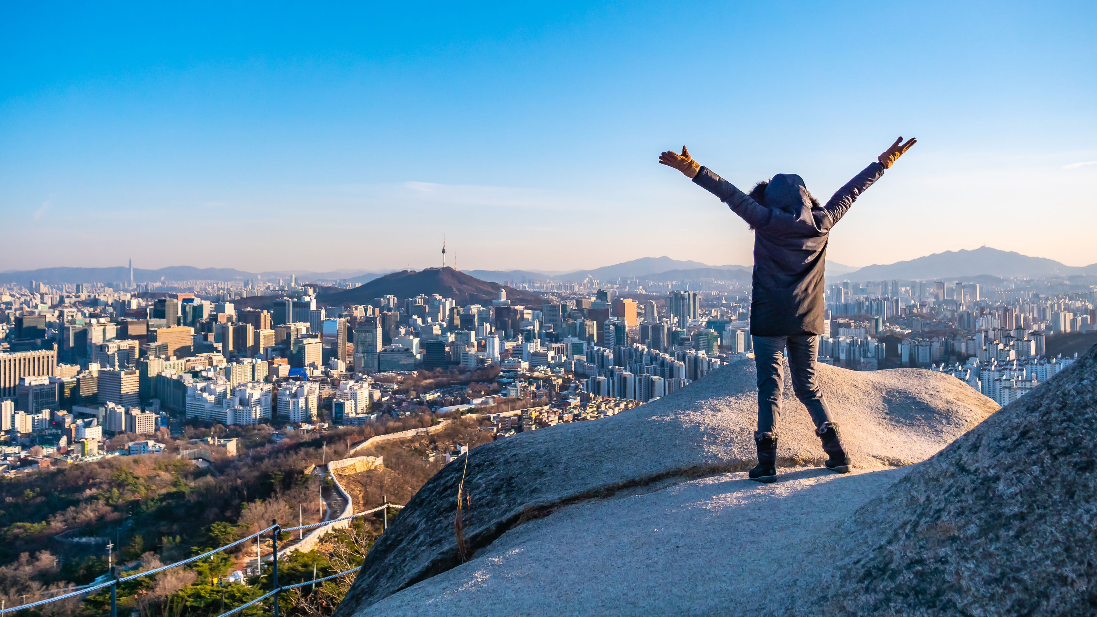 A person is standing on a large rock at the top of a mountain