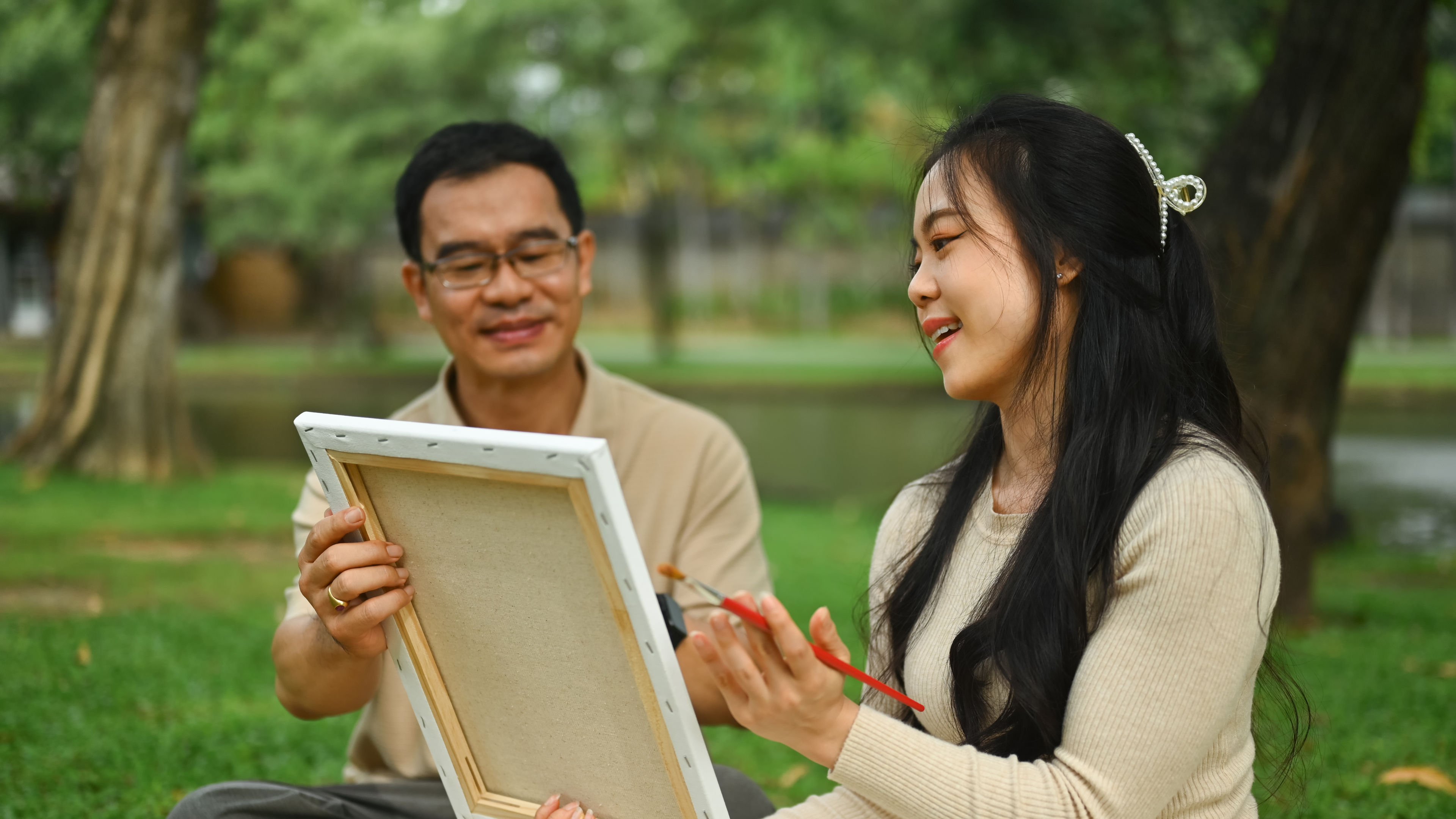 Wanita Asia yang bahagia dengan bapa melukis gambar dan menghabiskan masa bersama di taman hijau yang indah