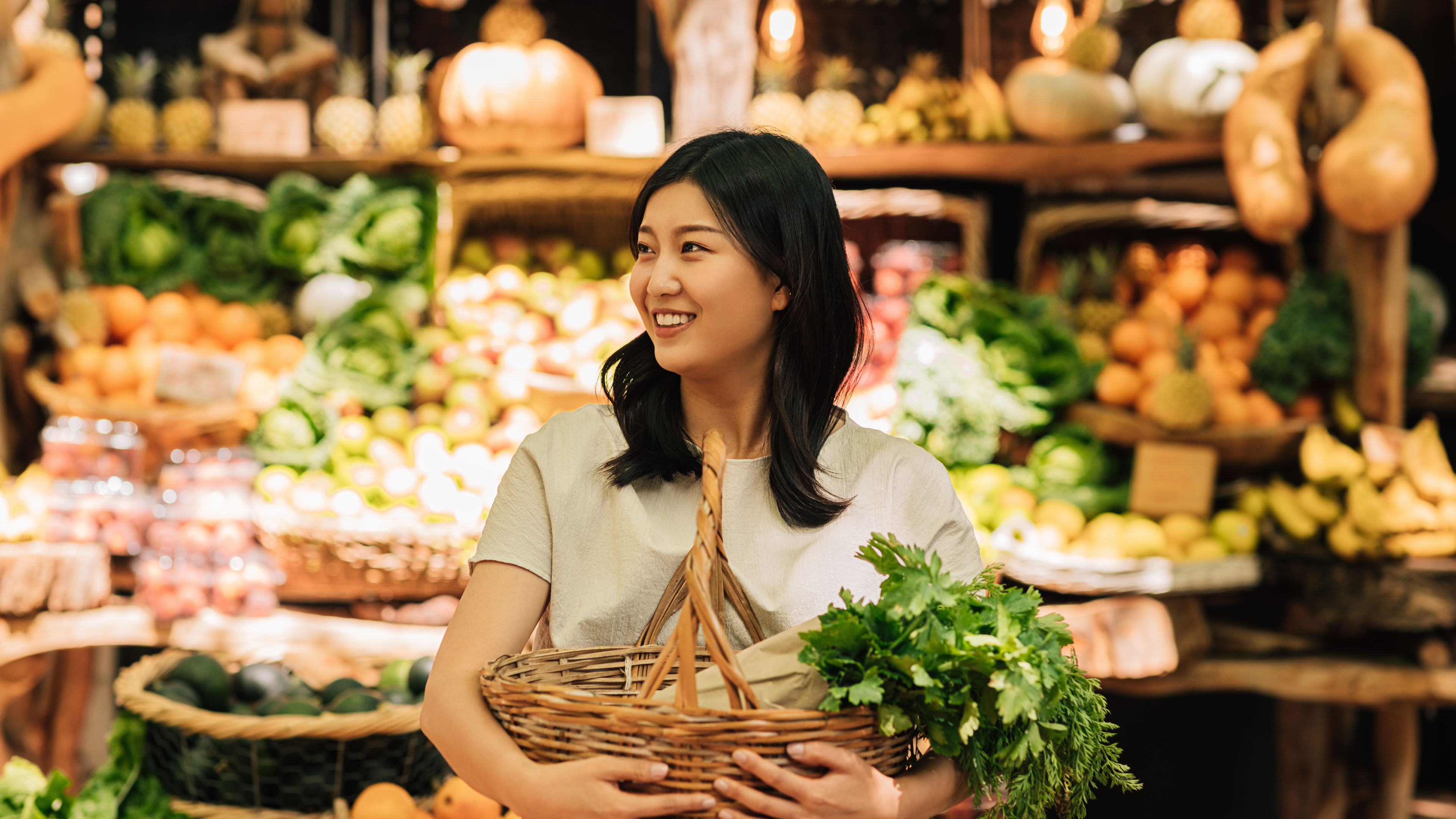 A smiling woman holding shopping basket with fresh vegetables 